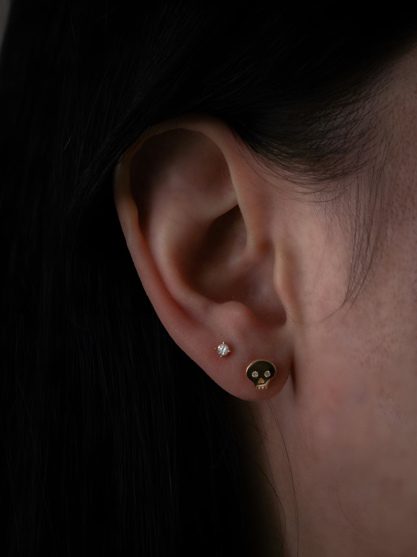 Yellow gold diamond skull stud earrings being worn on ear, front view
