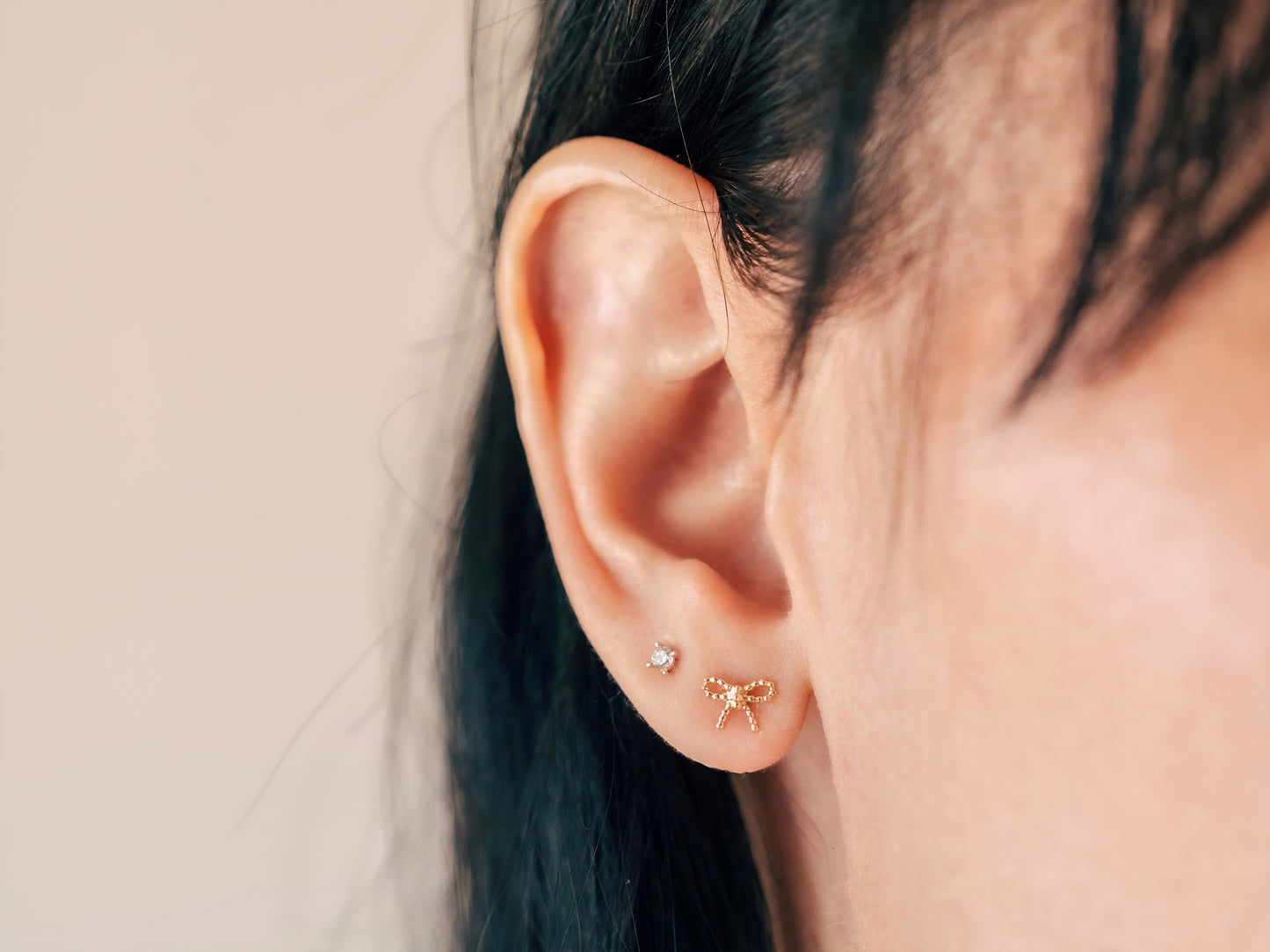 14k yellow gold, beaded bow stud earrings being worn on ear, side view