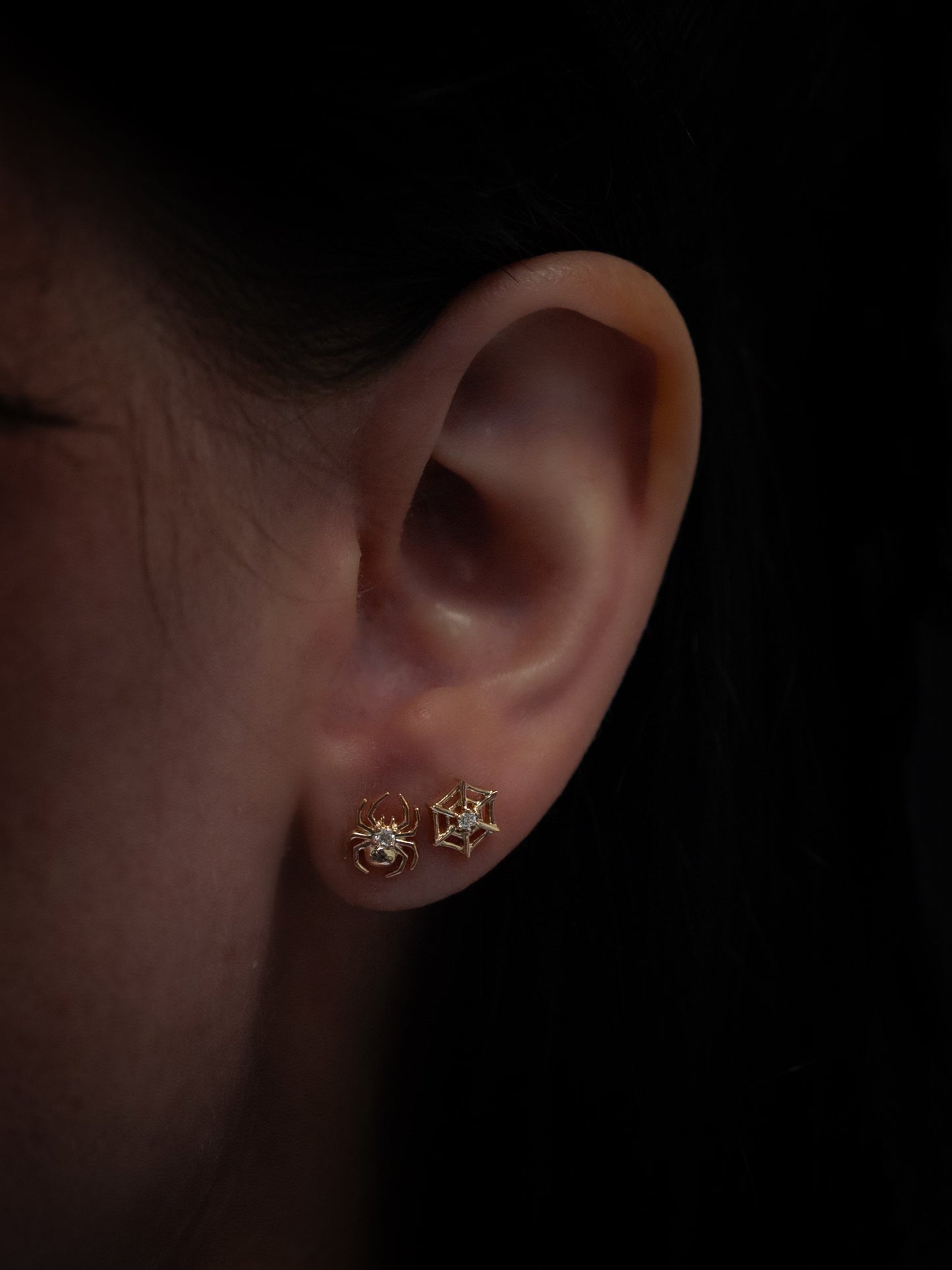 Yellow gold spider and spider web diamond stud earrings being worn on ear, front view