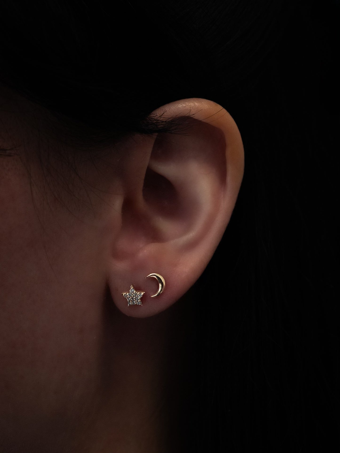 Yellow gold moon and star diamond stud earrings worn on ear, front view