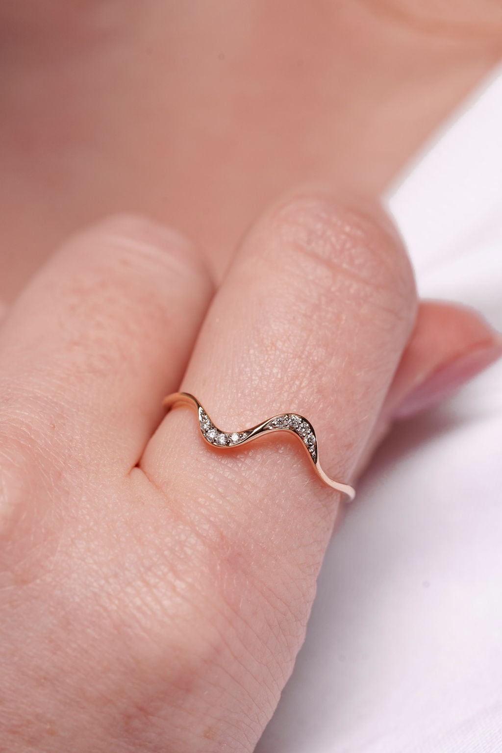 yellow gold ring with a wavy design on a finger against a blurred background